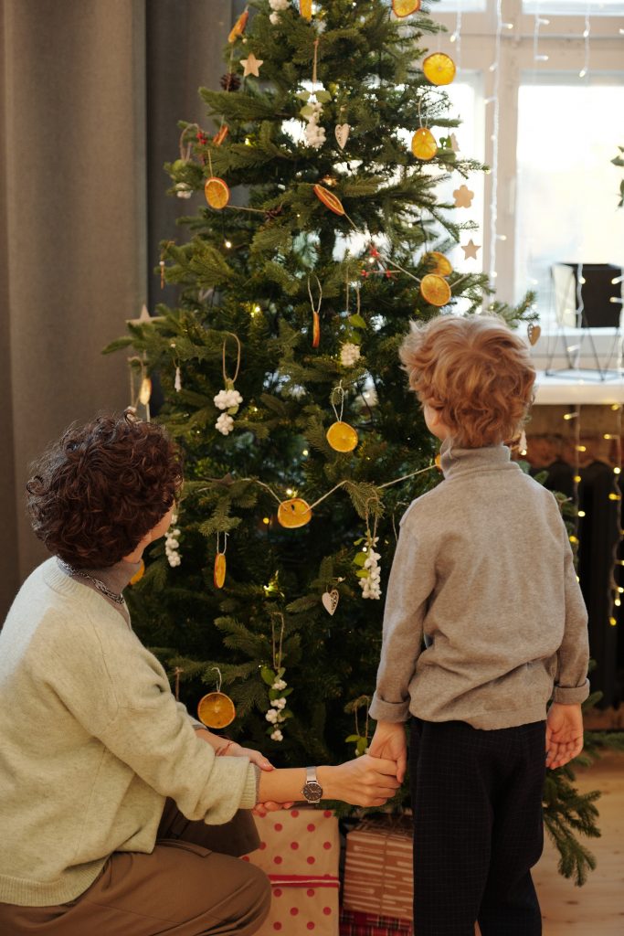 Mother and child holding hands looking at a decorated Christmas tree behind them.