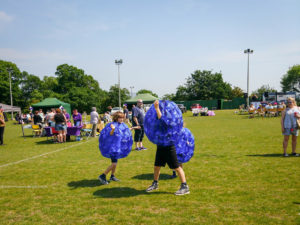 Three children wearing blue inflatable sumo suits playing on the grass.