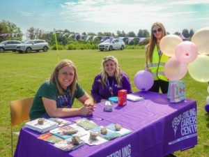 Three female members of staff sat at a table covered in a purple cloth, welcoming people to the event.