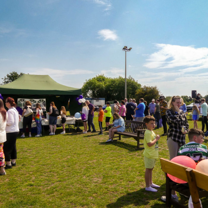 Crowds of people attending an open air event on a sunny day, with a tent serving food.