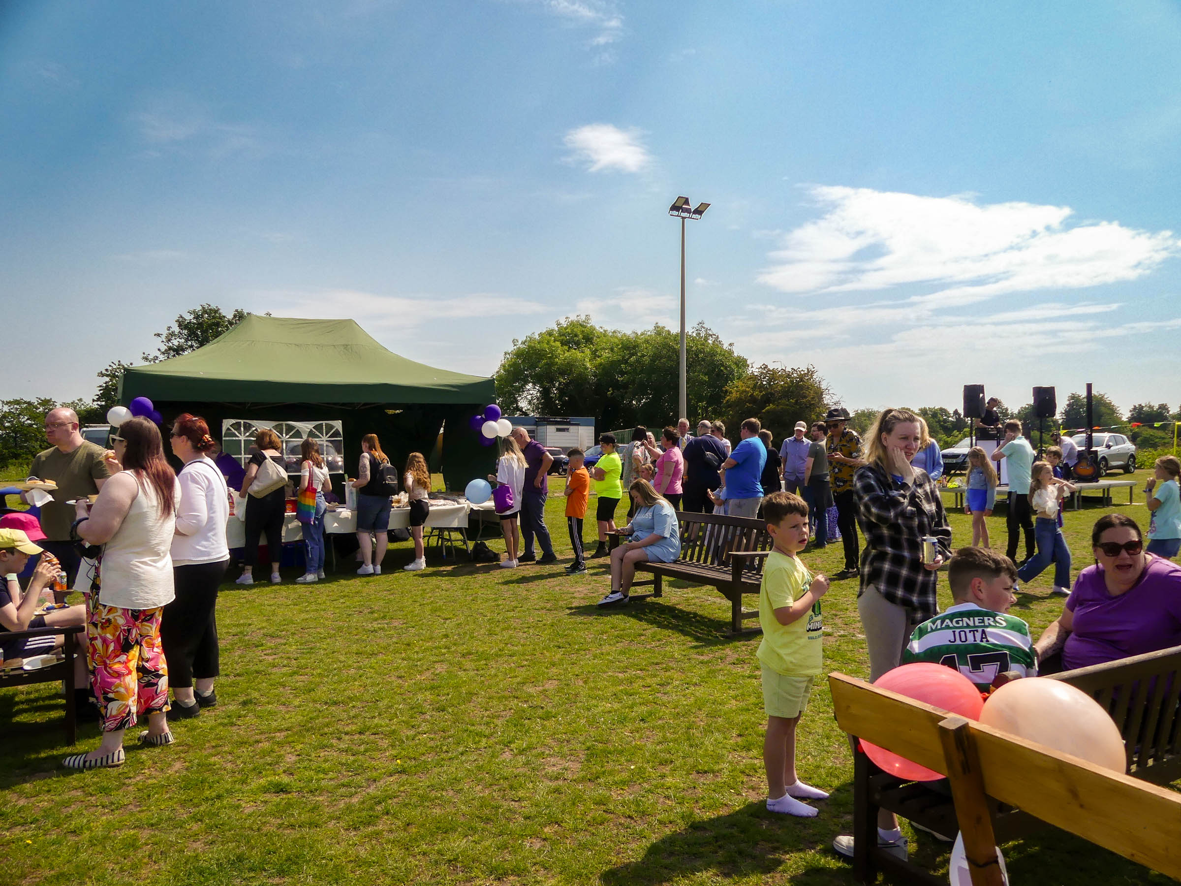 Crowds of people attending an open air event on a sunny day, with a tent serving food.