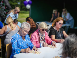 Three women sat at a table playing bingo in the sunshine.