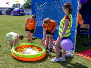 Three children and a female volunteer playing hook-a-duck in a paddling pool.