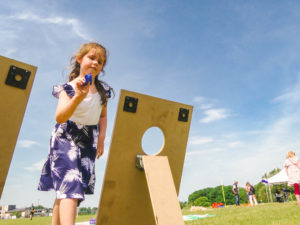 Young girl in blue and white dress throwing beanbags through a target.