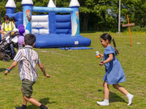Two young children playing on the grass in front of a bouncy castle.
