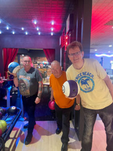 Three men holding bowling balls in a bowling alley