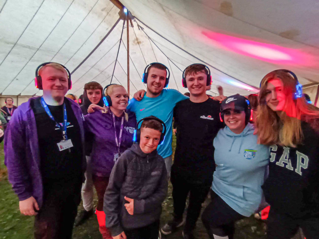 Group of young carers and leaders wearing headphones at a silent disco in a large tent.