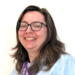 White lady with shoulder length brown hair and glasses wearing a light blue Young Carers hoodie